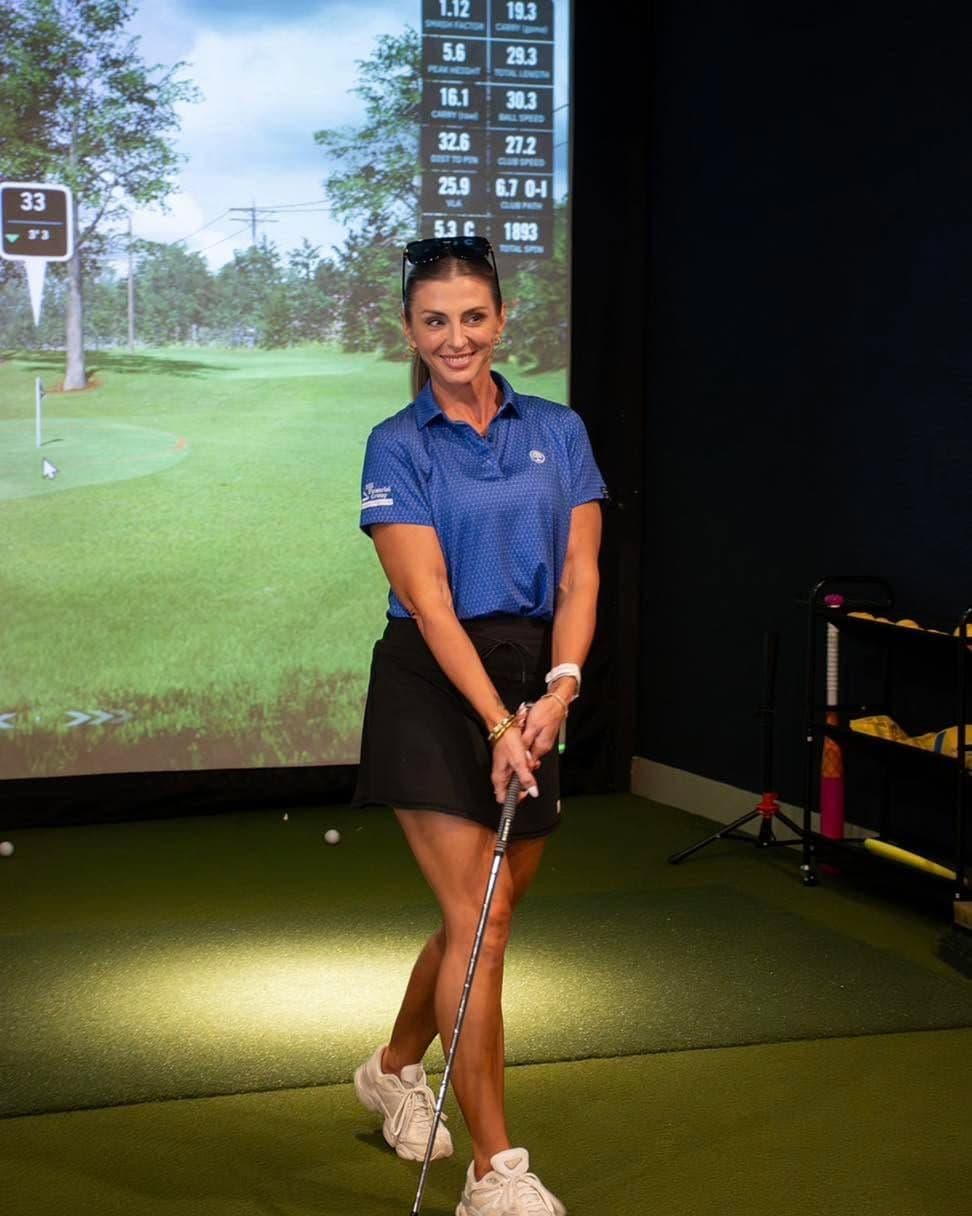 A golfer smiling mid-swing on a simulator bay