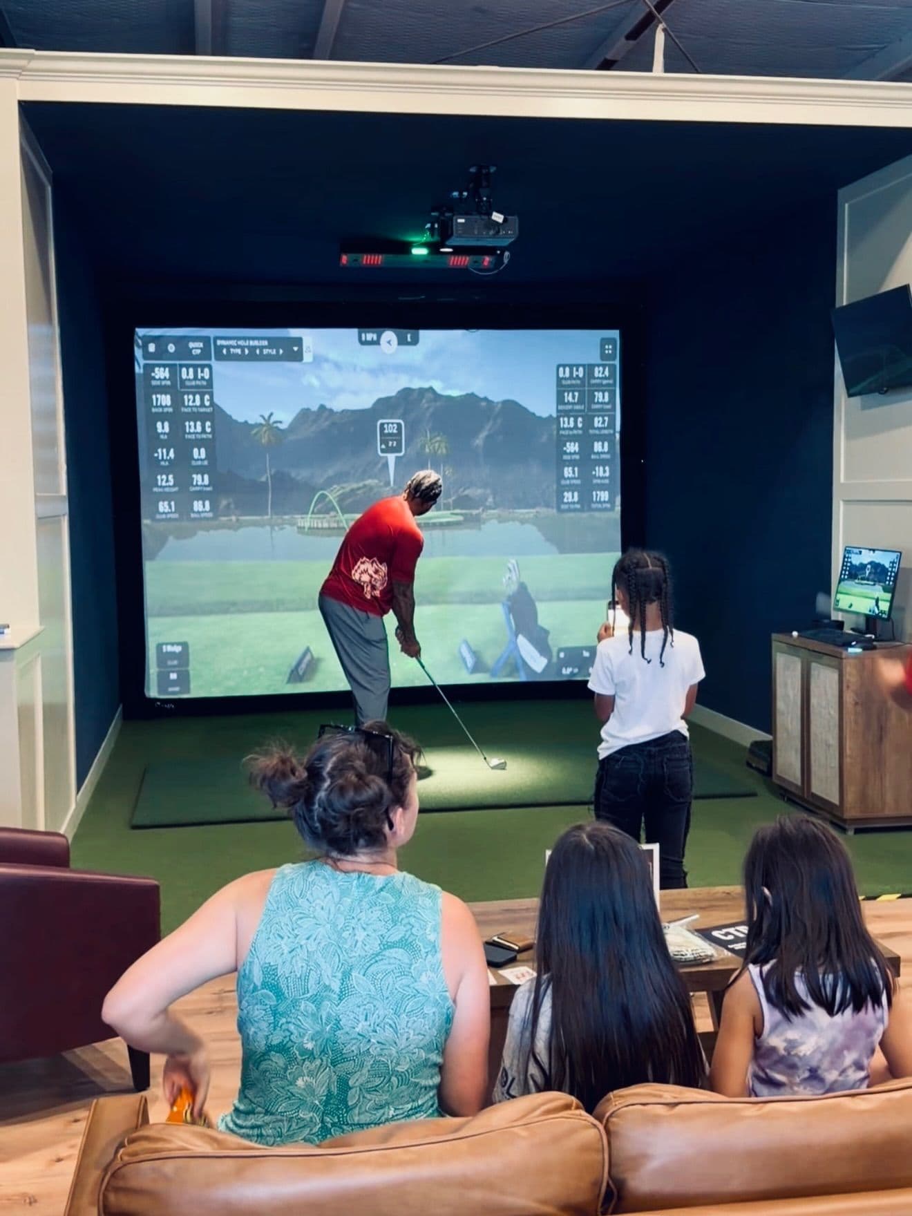Friends watching from the couch while a golfer tees off