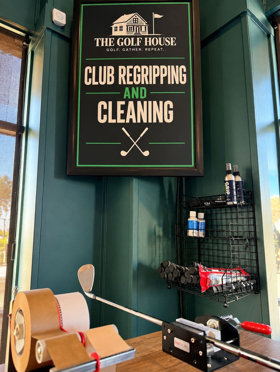 The Golf House club regripping and cleaning station: grip vise, tape, fresh grips, and the Club Regripping sign
